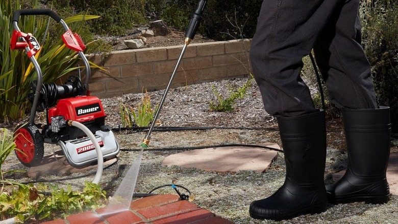 Person in black boots using the Bauer pressure washer on brick pavers