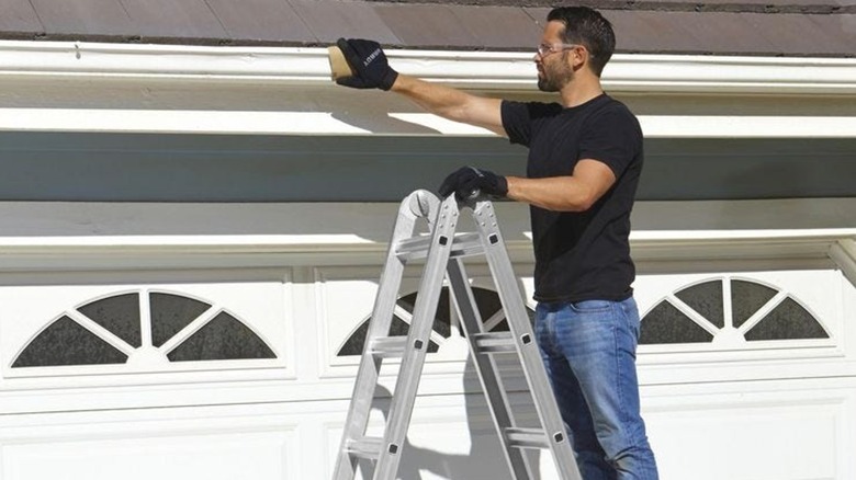 Man on ladder cleaning roof gutter