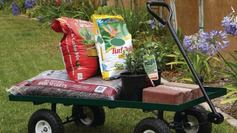 Utility cart with soil, plants, and bricks in a green yard