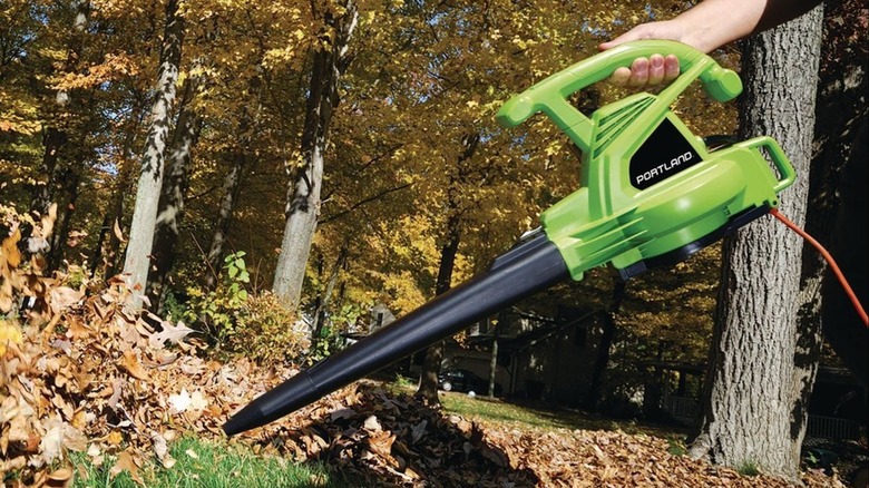 Green and black Portland blower blowing leaves in a wooded yard