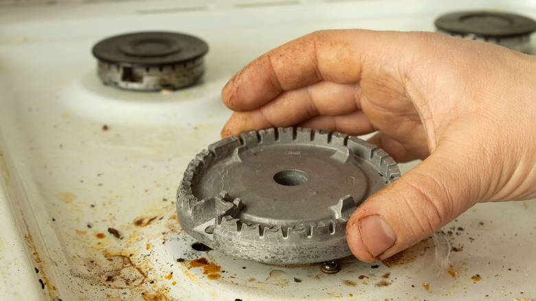 A hand holding a dirty stove burner head.