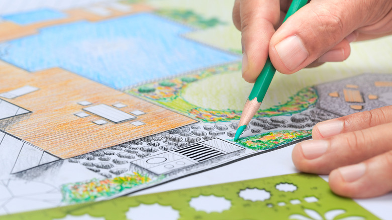 A person uses stencils and colored pencils to draw a garden design on paper.