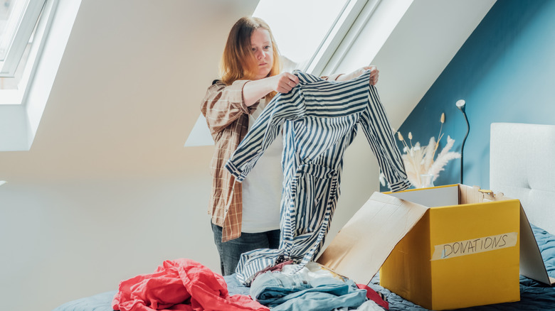 A woman looks at a striped shirt deciding whether to donate it or not.