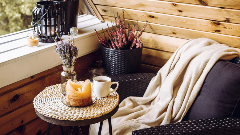 A back porch tastefully decorated for fall with an autumnal candle and throw blanket