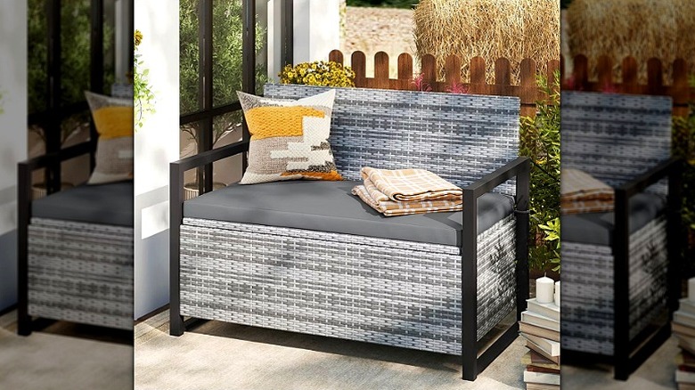 A gray faux wicker storage bench with black metal armrests on a patio.
