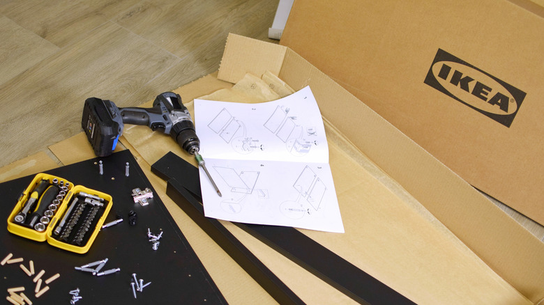 Open box of IKEA furniture with drill, screws, and instruction manual.