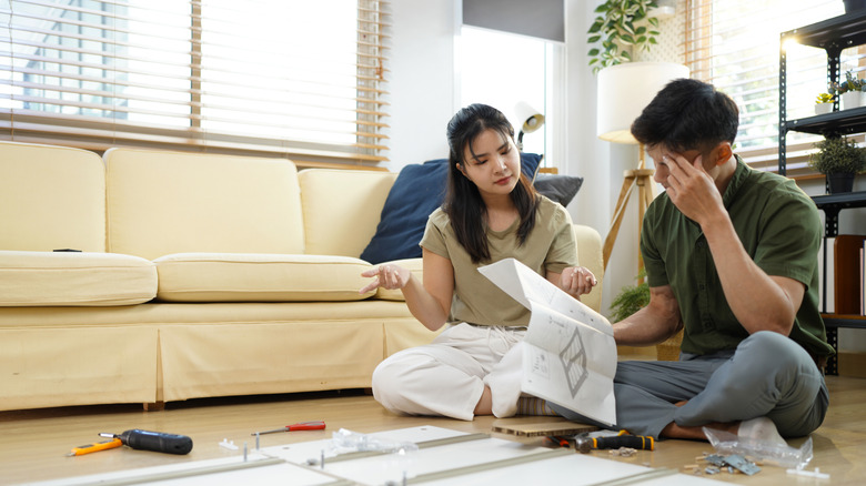 Couple confused assembling furniture in living room.