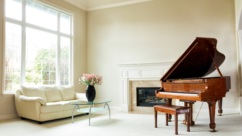 Living room with grand piano, fireplace, sofa and large window with bright daylight coming through.