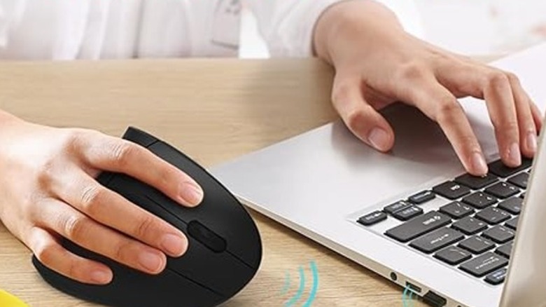 Hand holding a black vertical mouse near keyboard