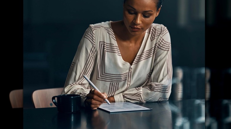 Woman working on a digital notebook with a cup of coffee nearby