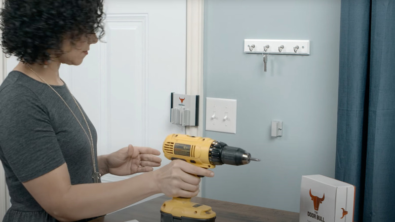 A woman in a grey shirt drilling to install a Door Bull.