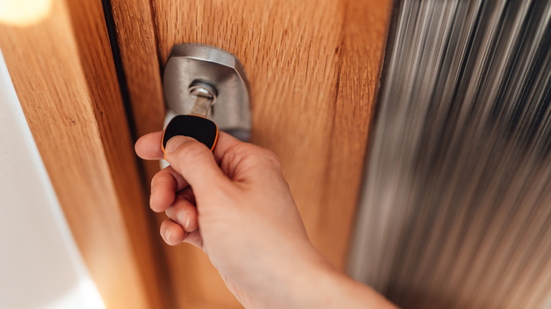 A person putting black key in wooden door.