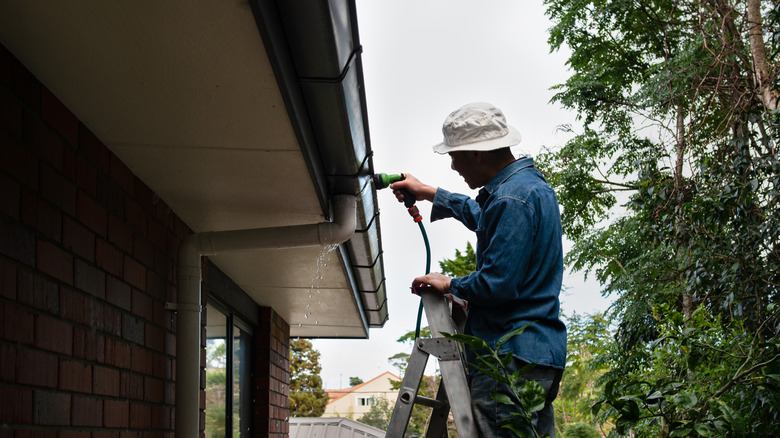 person using hose on gutter