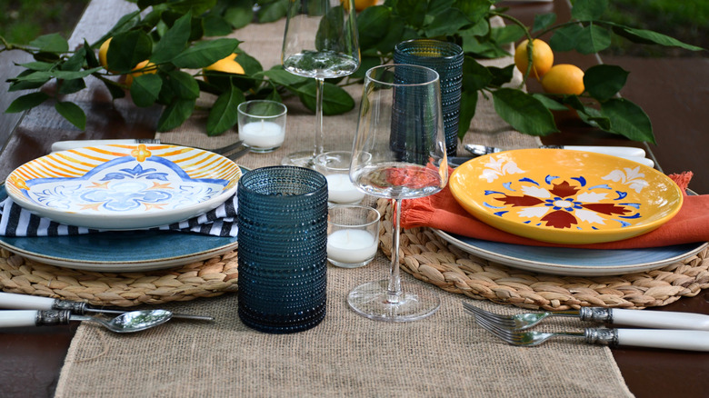 A burlap runner on a tablescape with glasses, citrus, and plates.