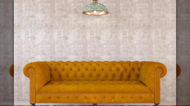 A goldenrod chesterfield sofa on a gray backdrop.
