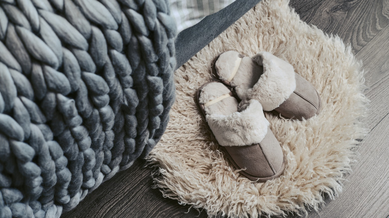Slippers sitting on a faux sheepskin rug under the bed.