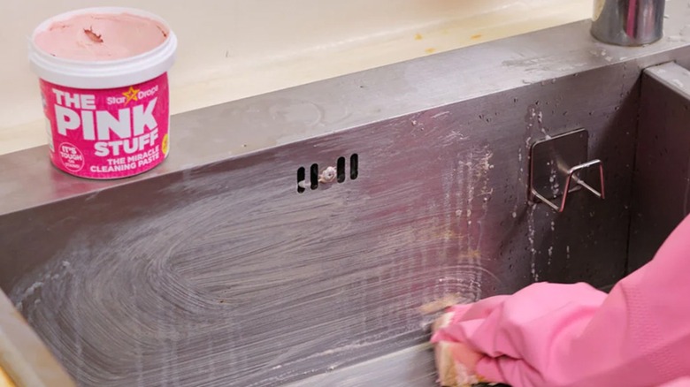 Gloved hand using The Pink Stuff Cleaning Paste to scrub sink