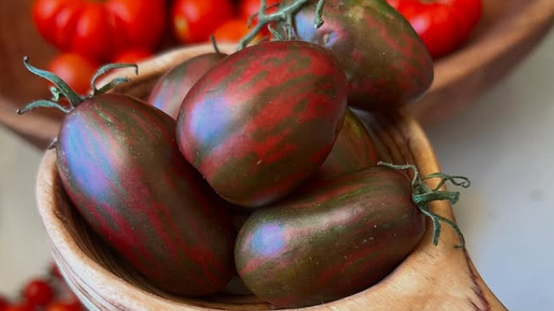 A wooden bowl filled with ripe 'Violet Jasper' cherry tomatoes.