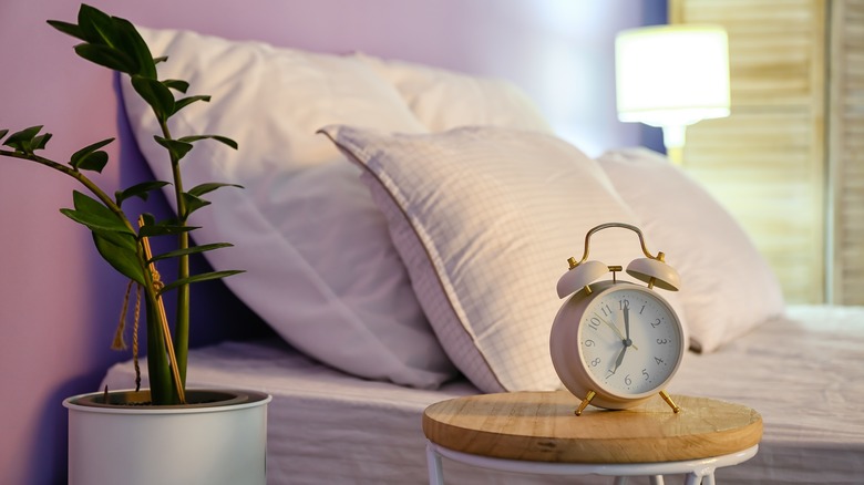 Pale mauve walls behind a cream double bed next to a bedside table