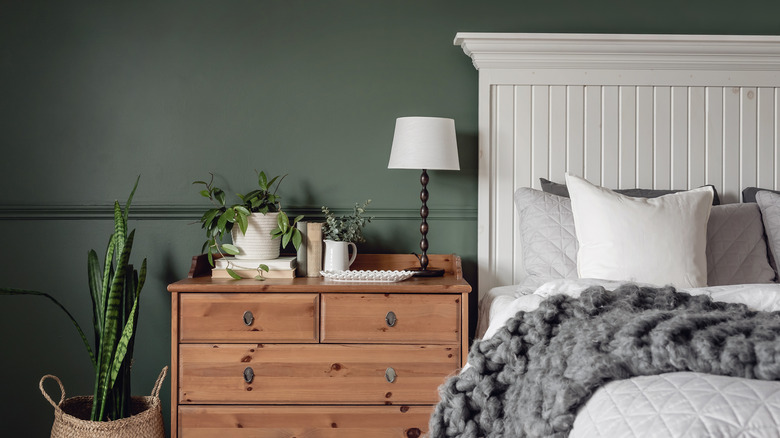 Neutral green walls behind a white bed with brown furniture and a plant