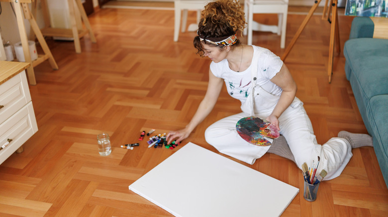 Woman sitting on the floor with paint supplies and canvas.