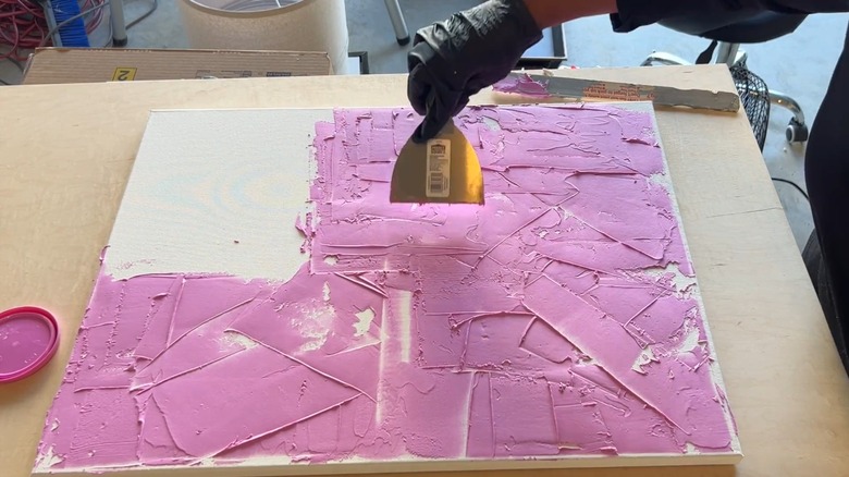 A woman coats a canvas with pink joint compound.