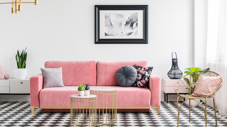 Black and white checkerboard floor with pink sofa and black framed picture on white wall