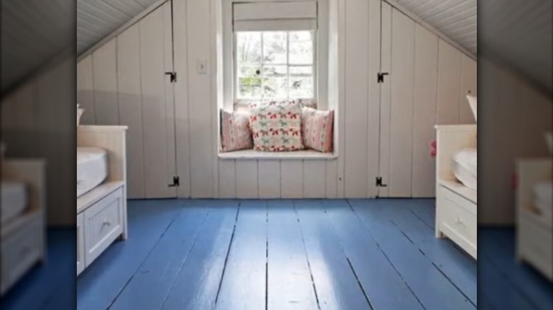 A attic with a blue painted floor and white walls, ceiling, and furniture