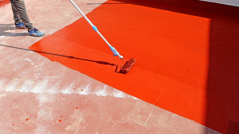 A person painting the floor orange with a roller