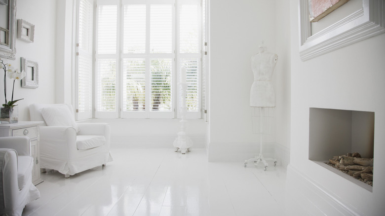A white room with white floors, white chairs, side table, and fireplace