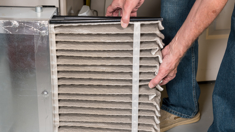 A man extracts a dirty filter from a furnace.