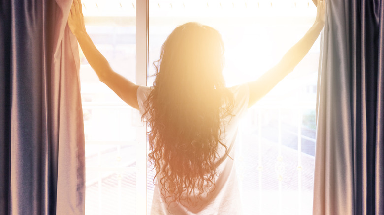 Woman opening drapes and letting sun in.