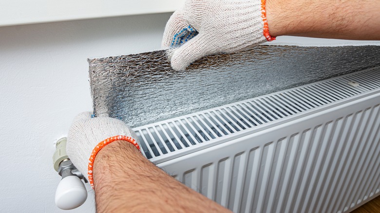 Man places a foil product behind a radiator to reflect its heat.