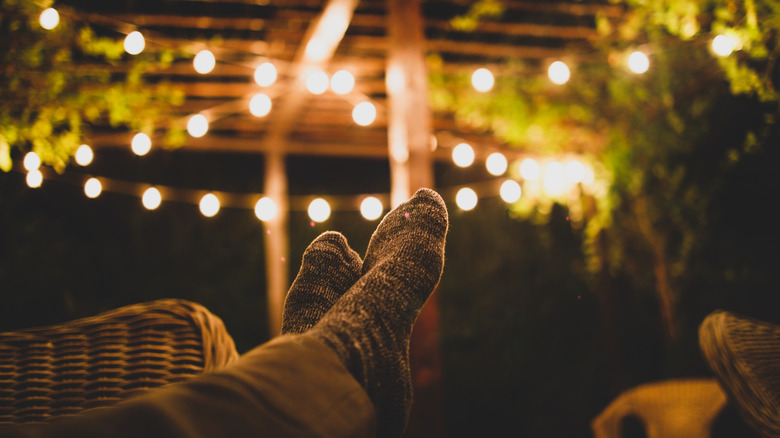 Man was his feet up in a dark backyard, barely illuminated by string lights above