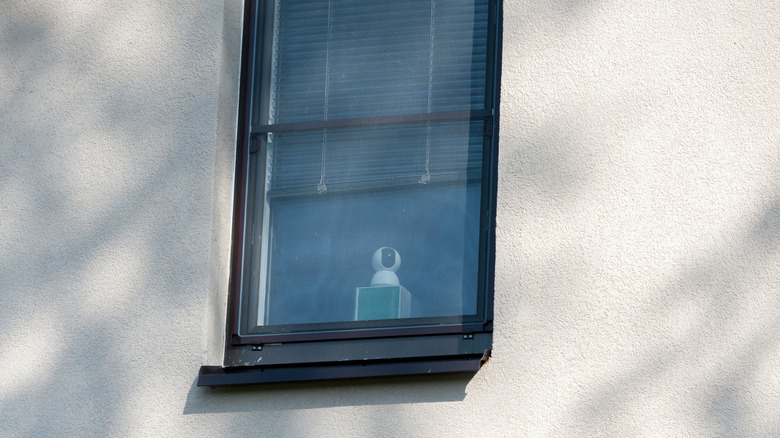 Window with blinds half up and a security camera behind the glass