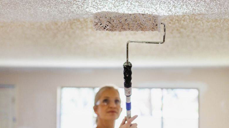 A woman uses a roller brush on a textured ceiling