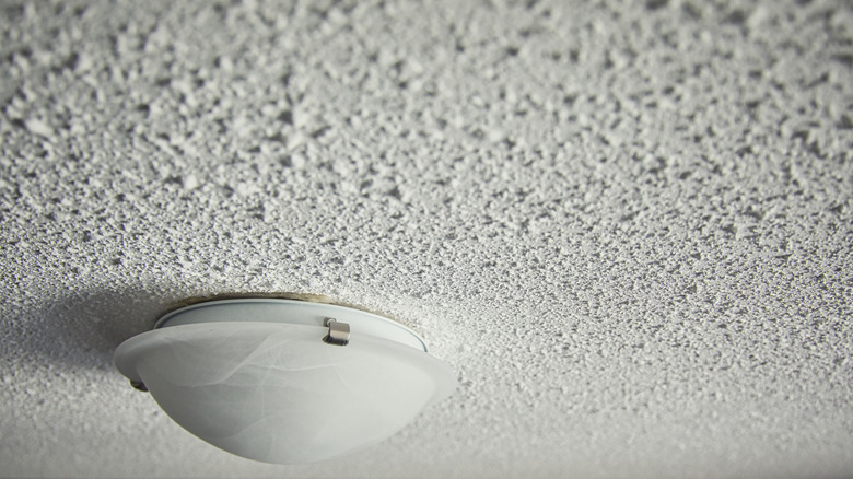 A white light fixture is installed on a popcorn ceiling