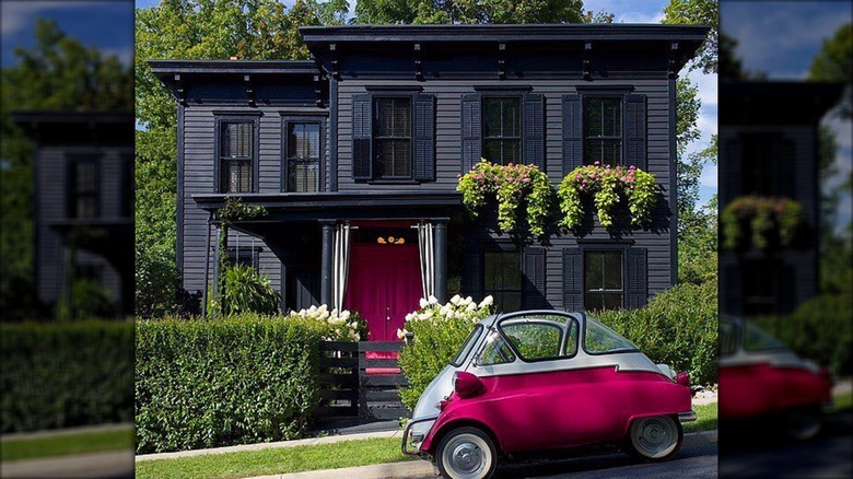 A retro hot pink car sits in front of a black house with a magenta front door