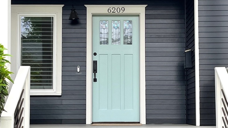 A light blue front door with stained glass windows pops against a house with black siding and white trim