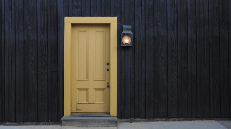 A mustard yellow front door stands out against a black stained wood house