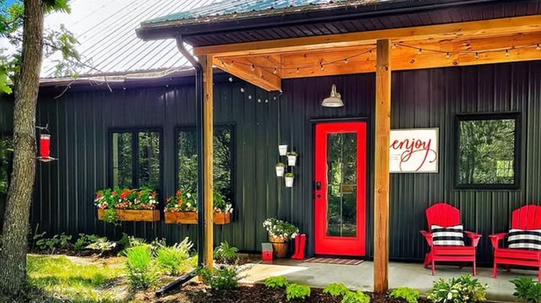 A sign that reads "Enjoy" hangs next to a red door on a black house
