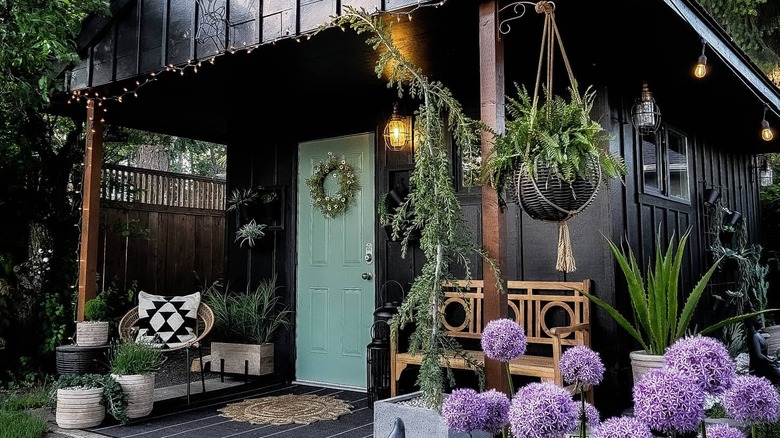 A patio in front of black house with a sage green door is decorated with fairy lights and lush plants