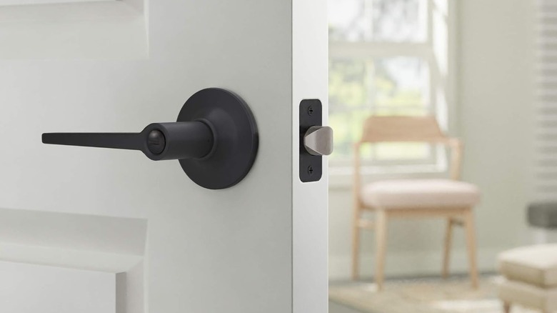 A white door with a matte black handle is open to reveal a beige chair near a window