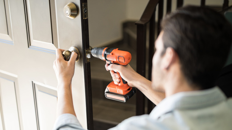 A man uses a power drill to install a door handle
