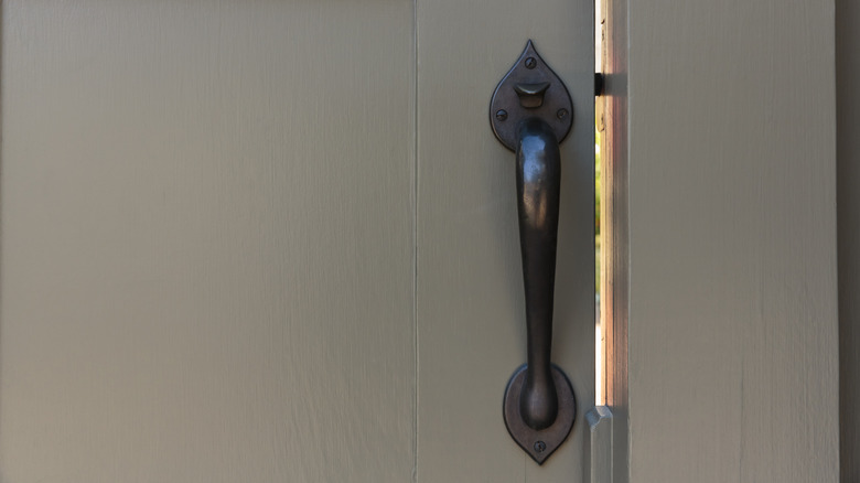 A black thumb latch handle is installed on a wooden gate door