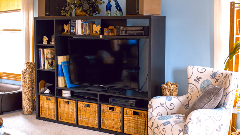 A room with a TV centered in a buy entertainment center with baskets and books