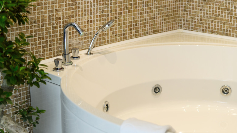 A large jet tub in a bathroom with small square tiles and a plant