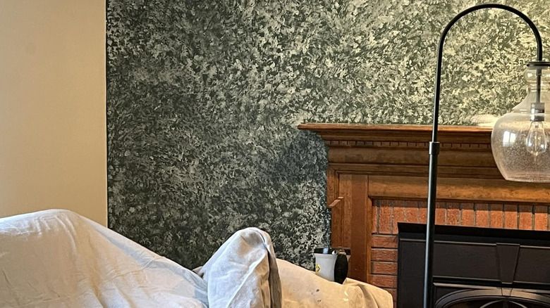 A feature wall with dark green sponge painting next to a wood and brick fireplace and a beige wall