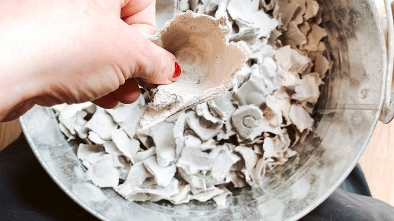 A pot filled with shredded egg cartons with a hand picking up a piece