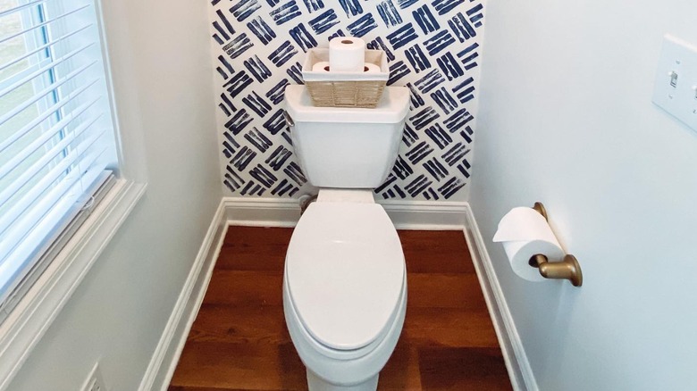 A water closet with a white toilet, basket on top, and toilet paper roll